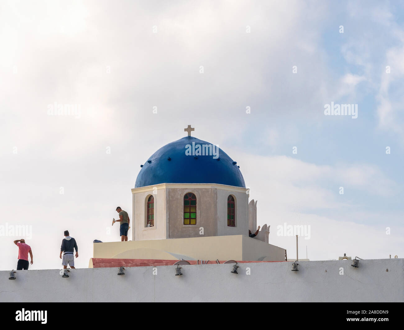1st Nov 2019 - Santorini, Greece. A worker applies plaster on the traditional Santorini church with a blue dome. Stock Photo