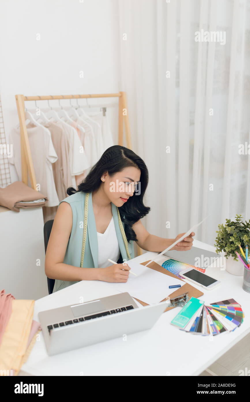 Portrait of young Asian fashion designer sitting at the desk in front ...