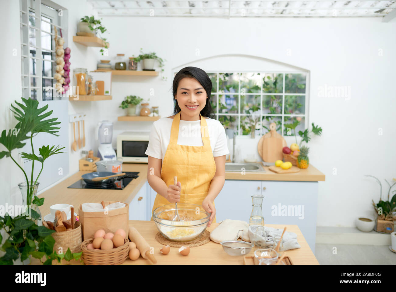 female mixing flour with eggs while using whisk. She is cooking bakery in domestic atmosphere Stock Photo