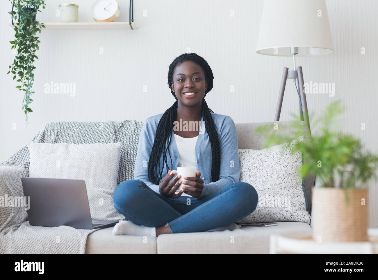 Afro woman freelancer sitting on couch with coffee and laptop Stock Photo