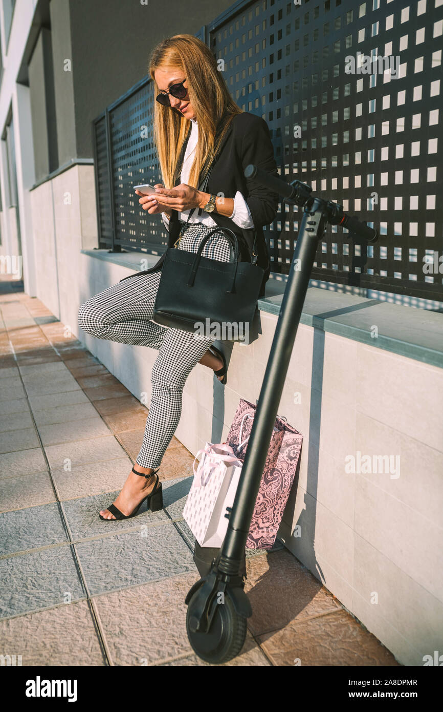 Woman with mobile and her scooter and shopping bags next Stock Photo