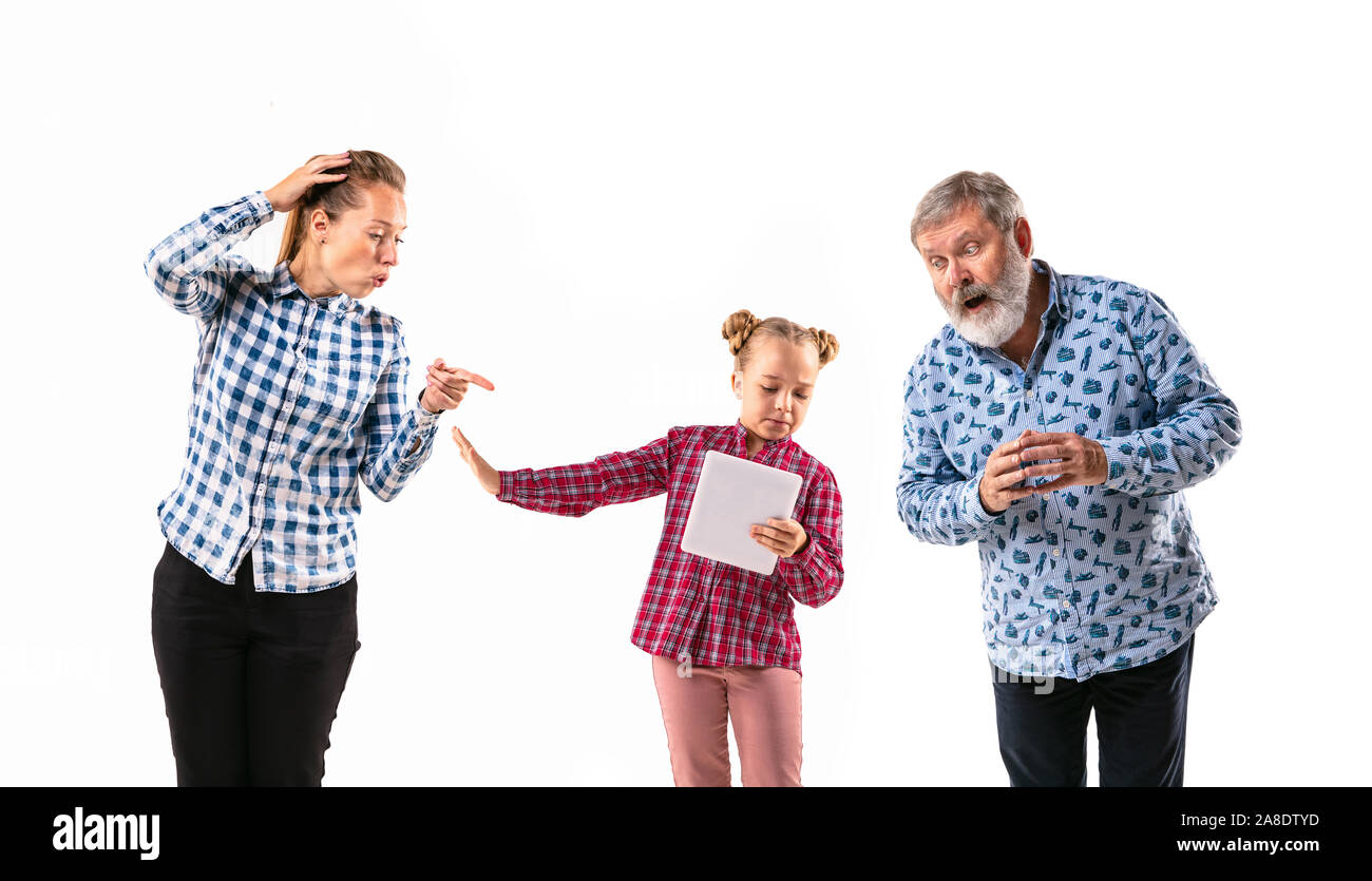 Family members with one another on white studio background. Concept of human emotions, expression, conflict of generations. Woman, man and little girl. Total control by parents. No freedom. Stock Photo