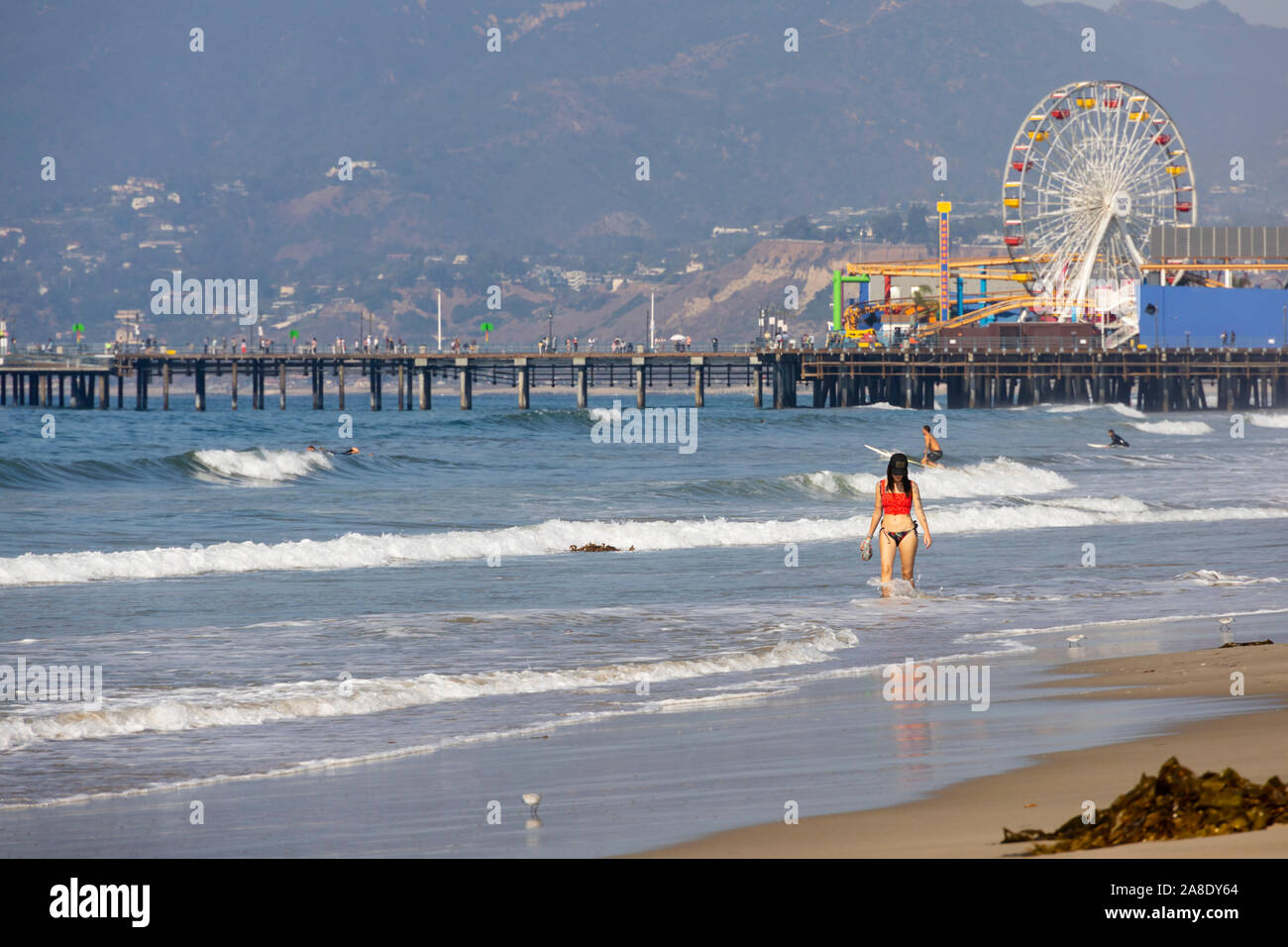 Girl in red top and bikini walking through the sea on the beach, Santa