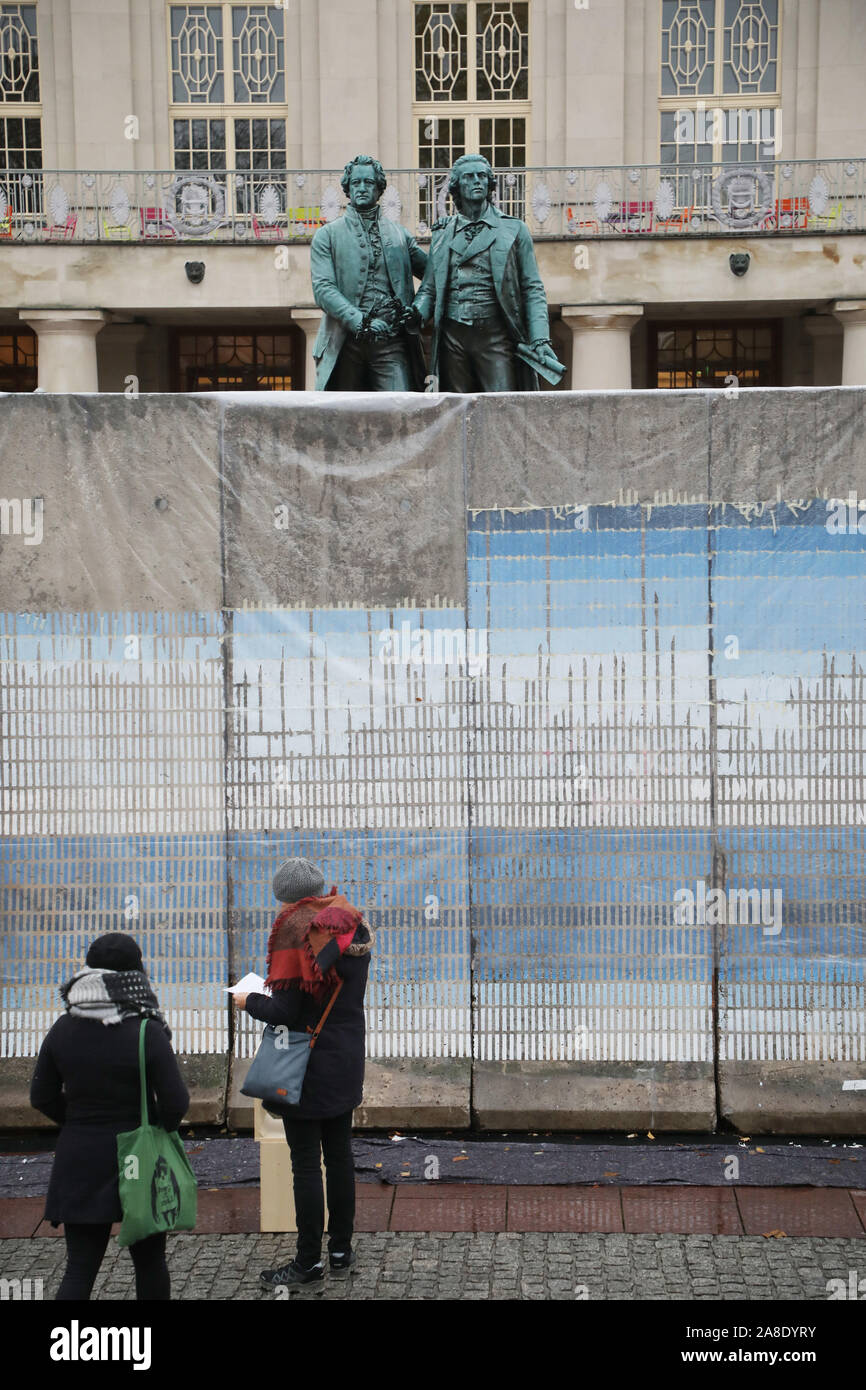 Weimar, Germany. 08th Nov, 2019. Passers-by walk along the wall  installation "Horizons" in memory of the fall of the Berlin Wall in 1989 in  front of the Goethe Schiller Monument and the