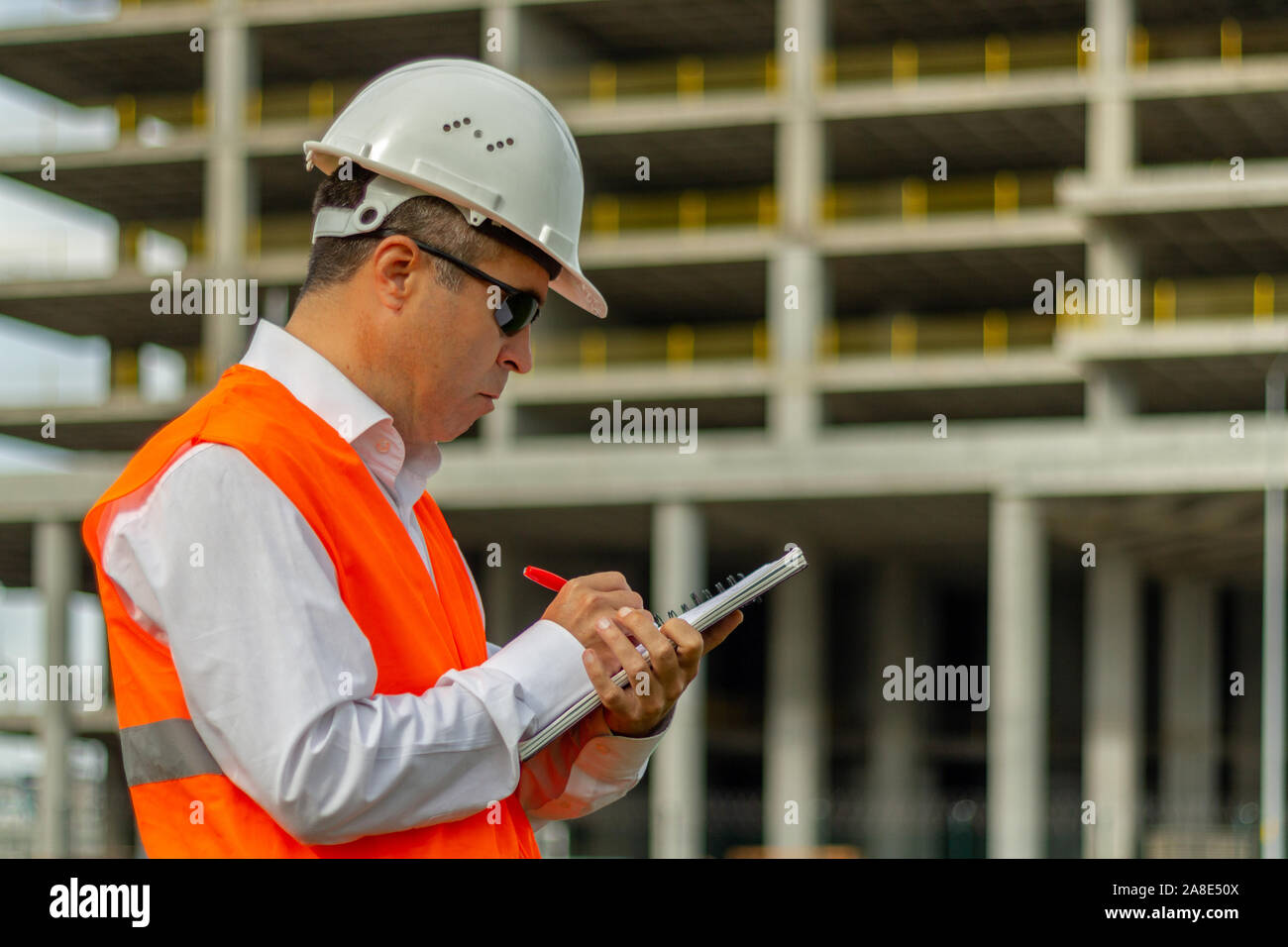 Construction engineer man in shirt and tie with safety helmet and vest works at construction site. Concept of people working in industrial field Stock Photo