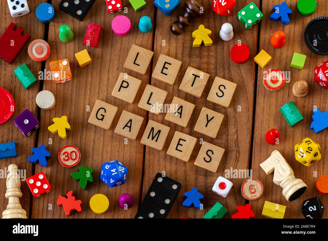 Lets Play Games" spelled out in wooden letter tiles. Surrounded by dice,  cards, and other game pieces on a wooden background Stock Photo - Alamy