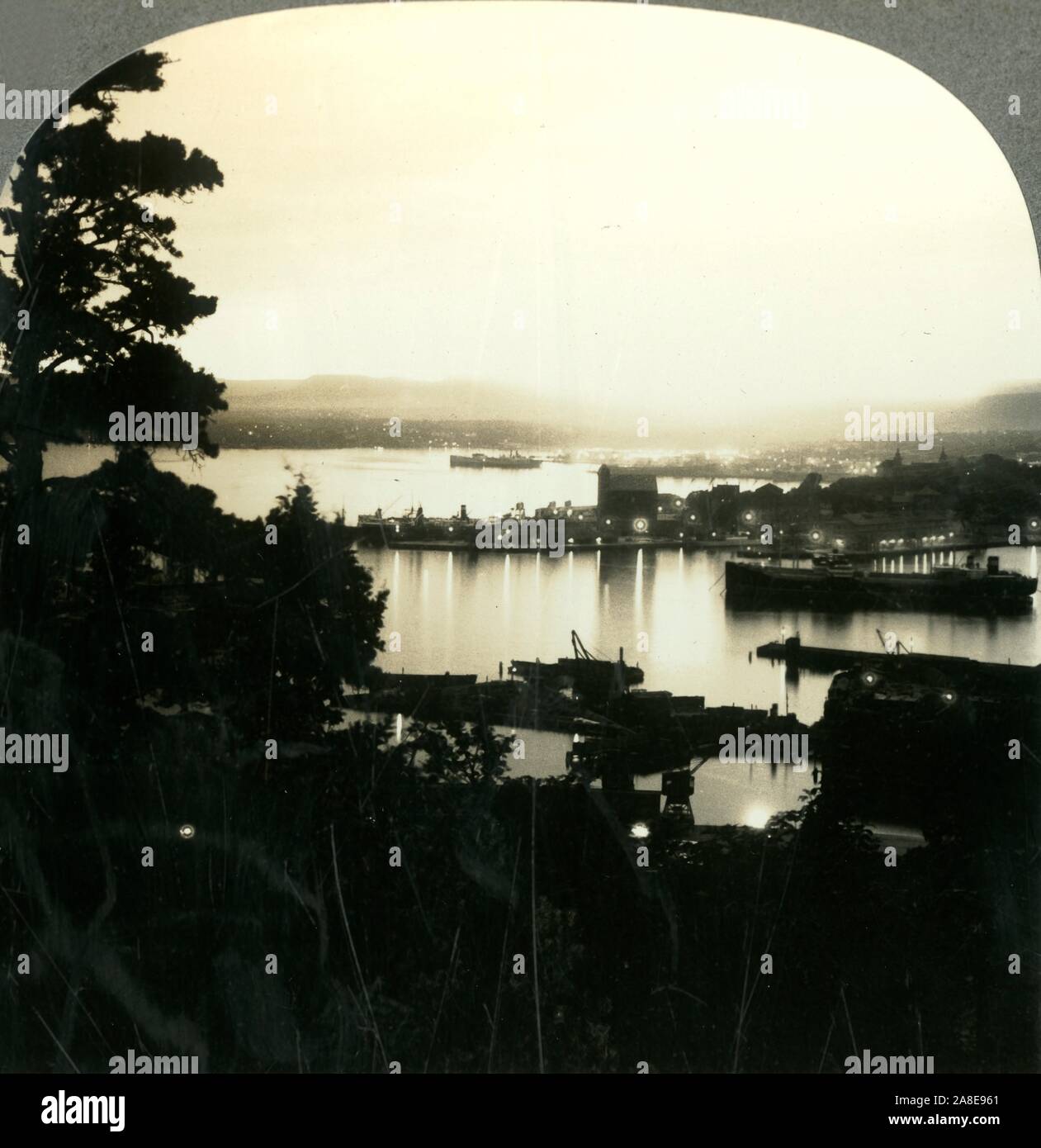 'The Lights of Oslo and the Harbor on a Summer Night, Norway', c1930s. During the summer months in the Northern Hemisphere, the sun is visible during the night. From &quot;Tour of the World&quot;. [Keystone View Company, Meadville, Pa., New York, Chicago, London] Stock Photo