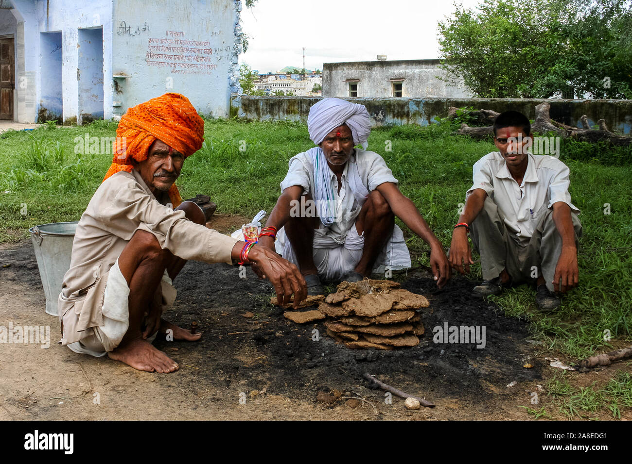 Pushkar, Rajasthan, India: three Indian men with turbans sitting on their heels in front of a pile of dry dung ready for fire. Stock Photo