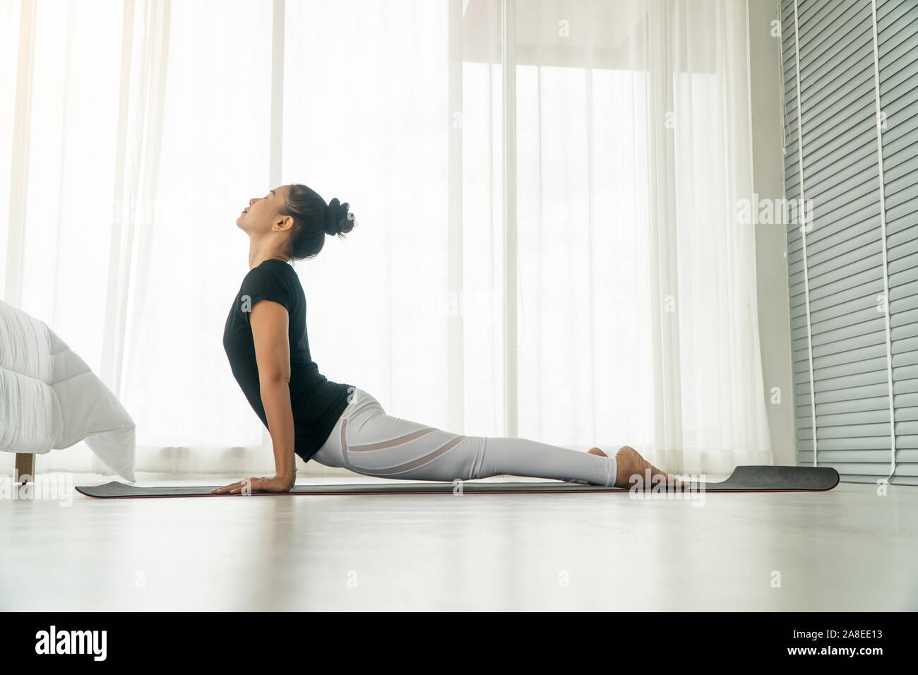 Middle aged women doing yoga in bedroom at the morning, adho mukha svanasana pose. Concept of exercise and relaxation in the morning. Stock Photo