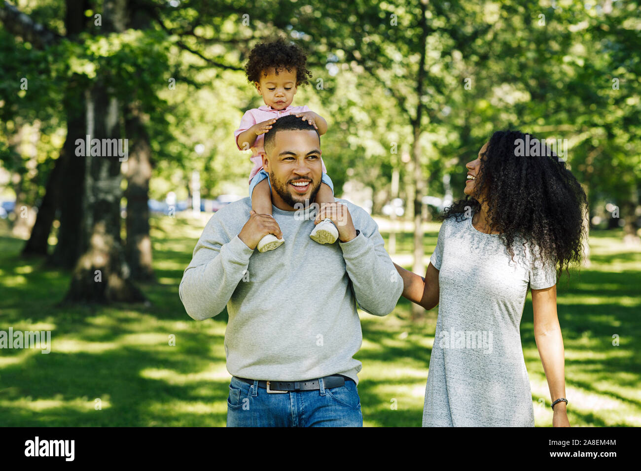 Two parents and their son walking outside. Mother looking on her son sitting father's shoulders. Stock Photo