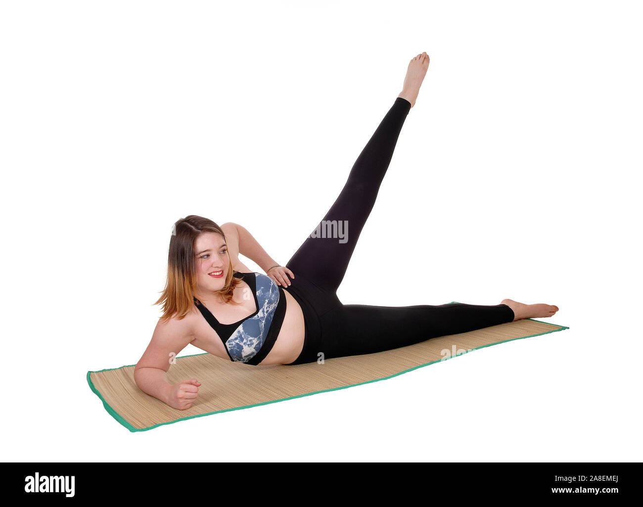 A beautiful young woman exercising on the floor with one leg up in a sports outfit, isolated for white background Stock Photo