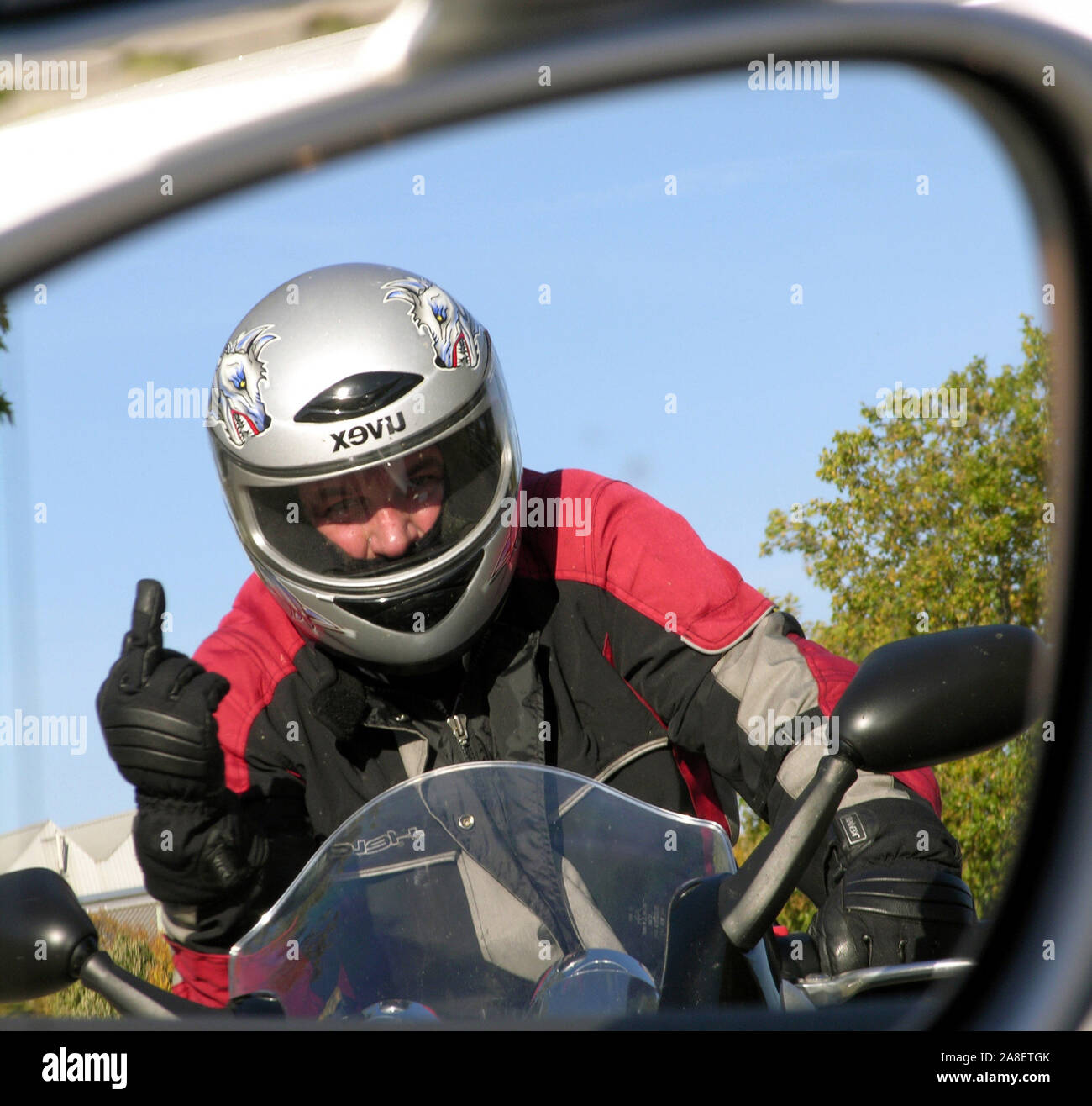 Verärgerter Motorradfahrer zeigt den Mittelfinger, Autofahrer sieht das im Spiegel seines Autos, Stock Photo