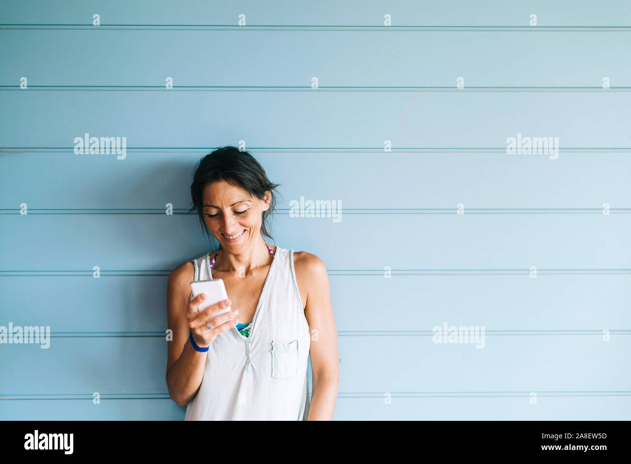 Beautiful woman leaning on a wood wall while using a smartphone Stock Photo
