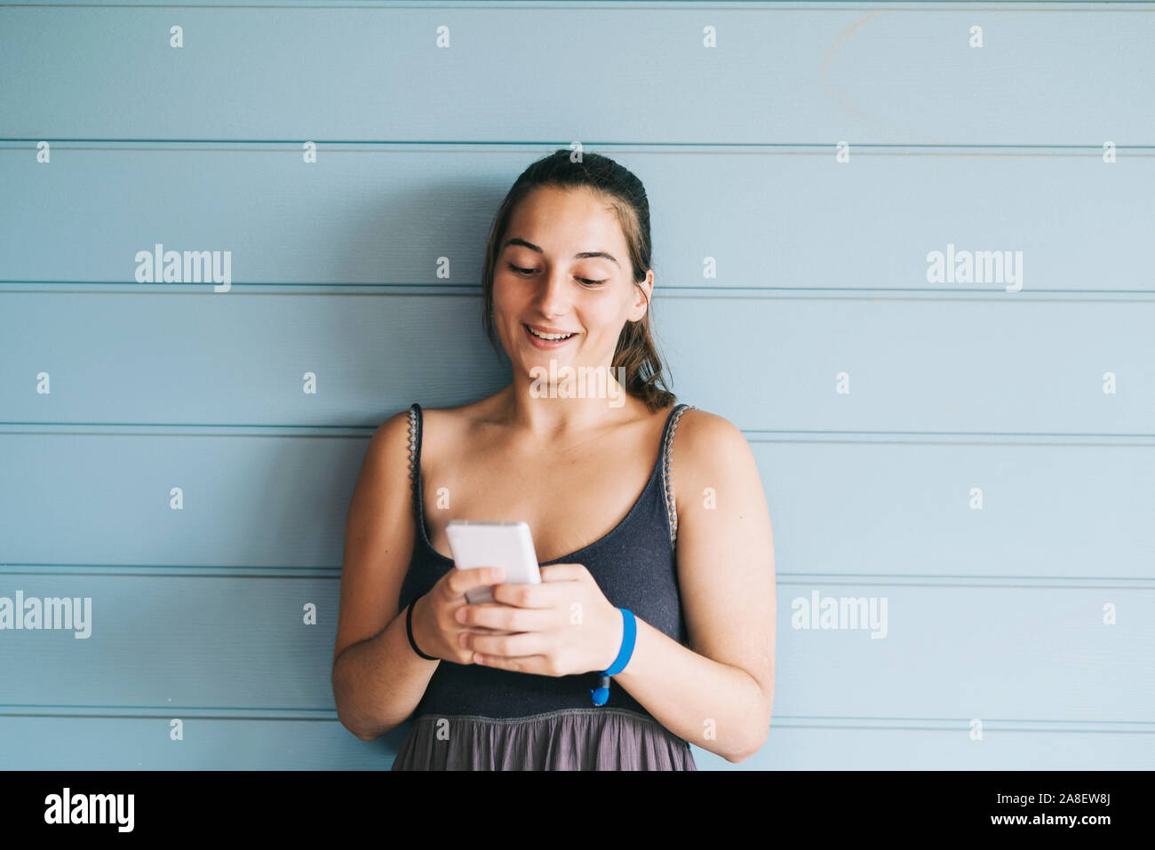 Beautiful woman leaning on a wood wall while using a smartphone Stock Photo