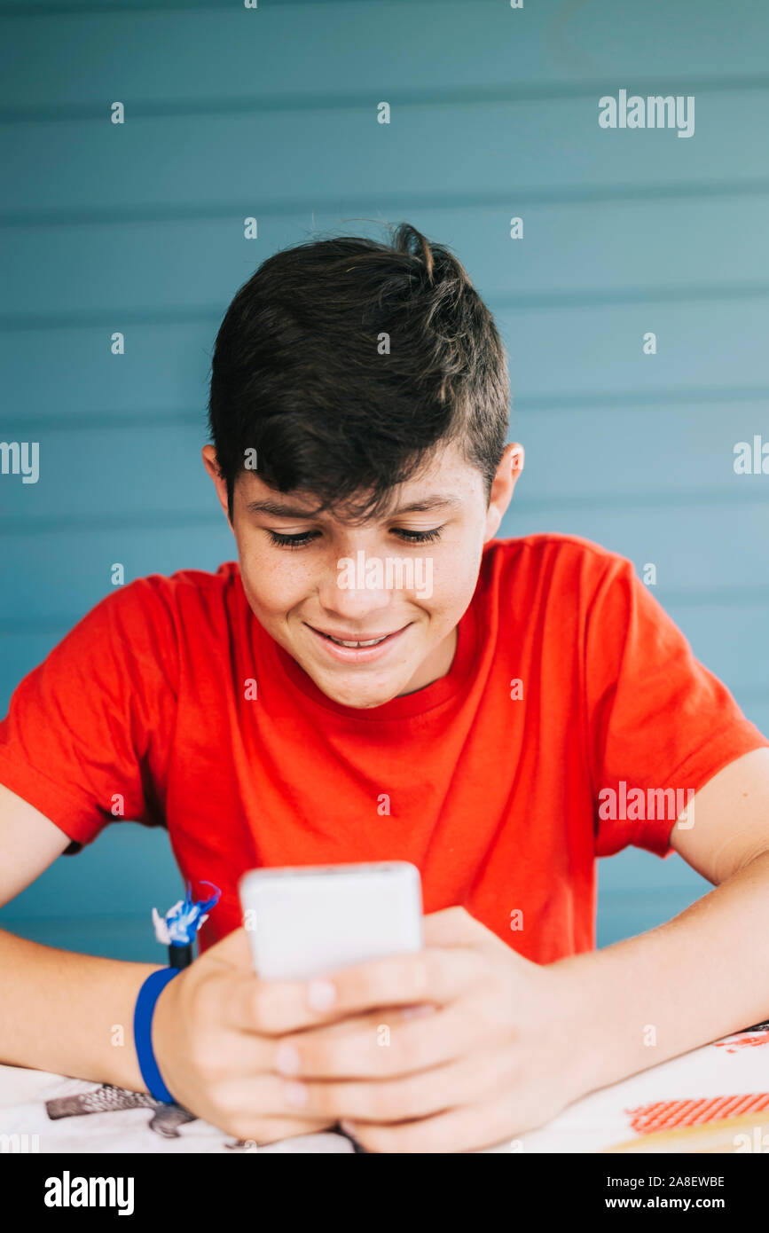 Handsome Caucasian 13year old boy wearing red tshirt sitting outdoors using electronic gadget