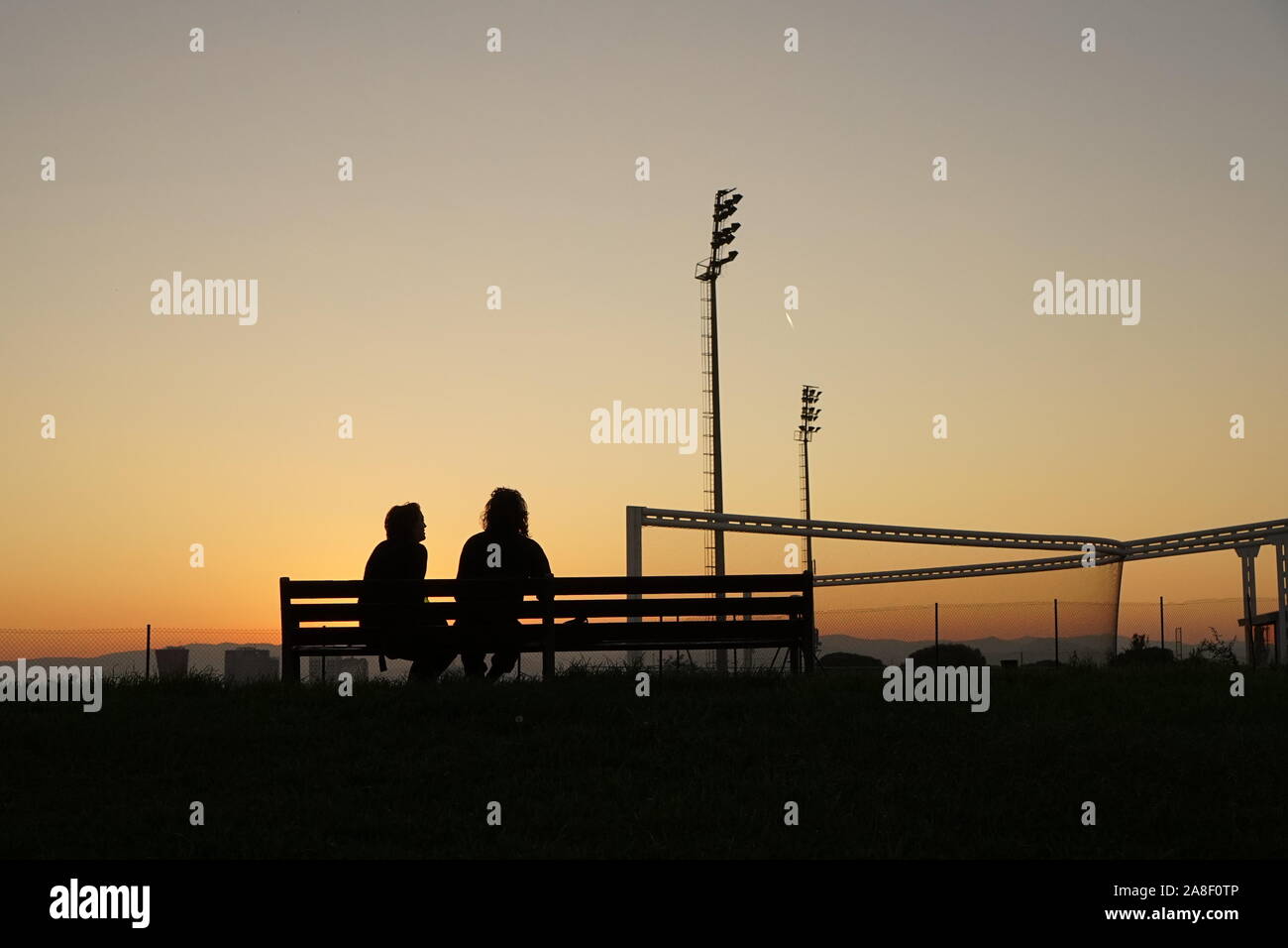 A couple sitting on a bench in the sunset at the edge of Barcelona city Stock Photo