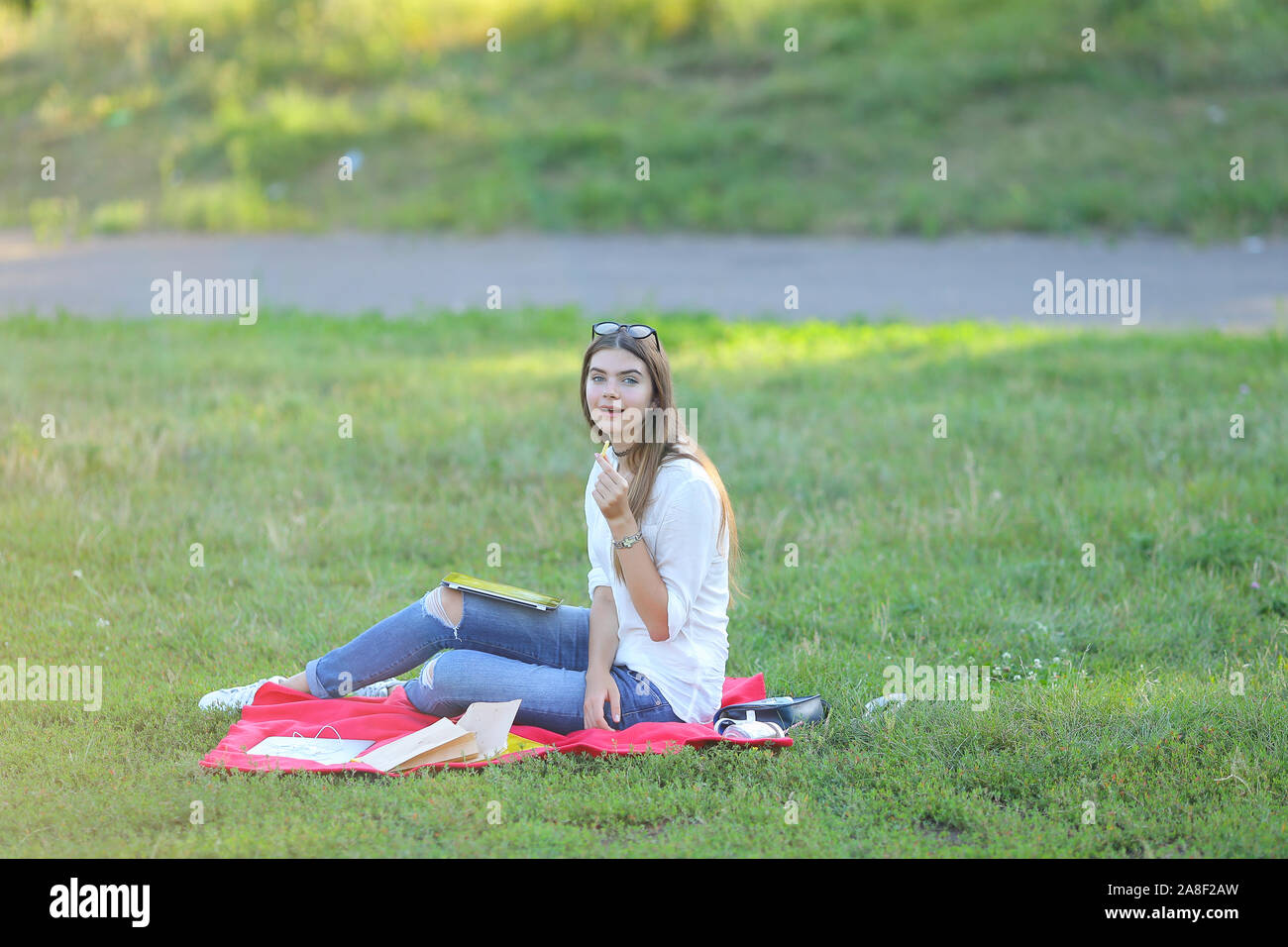 young girl sitting on the grass in the park and works at a laptop and ...