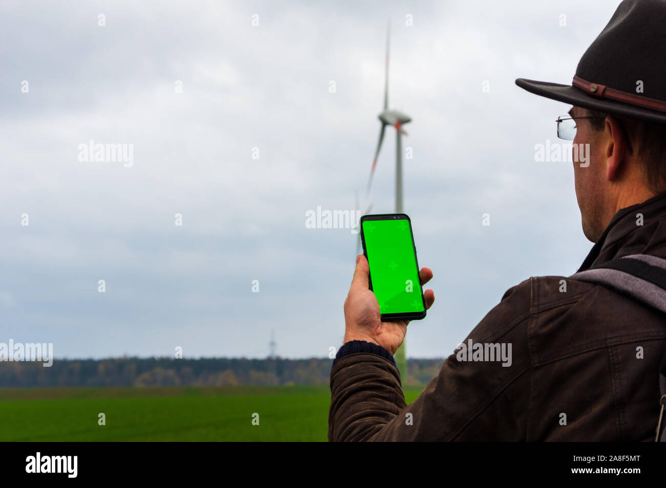 man using his smartphone in front of out of focus wind turbines. Accessing iot wind energy network with a cell phone. Using mobile phone outdoors Stock Photo
