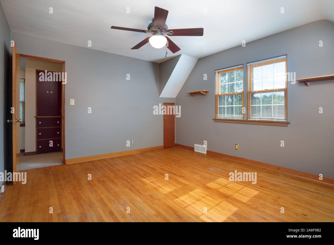 An old, plain grey room with no furniture and hardwood floors looking towards the hallway. Stock Photo