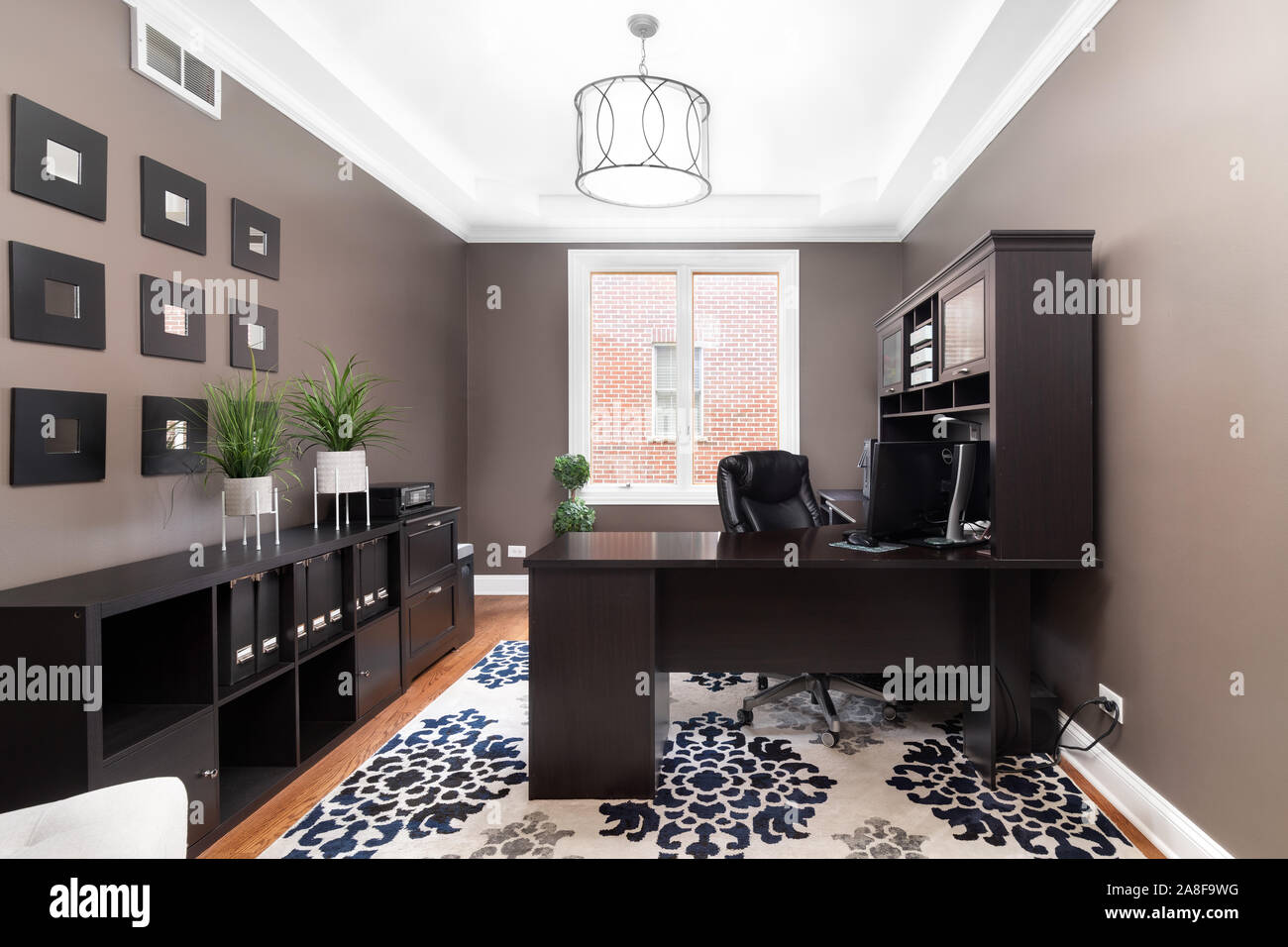 Home office in a Chicago condo with dark brown walls and a dark colored wrap around desk. Decorations fill the rest of the room comfortable room. Stock Photo