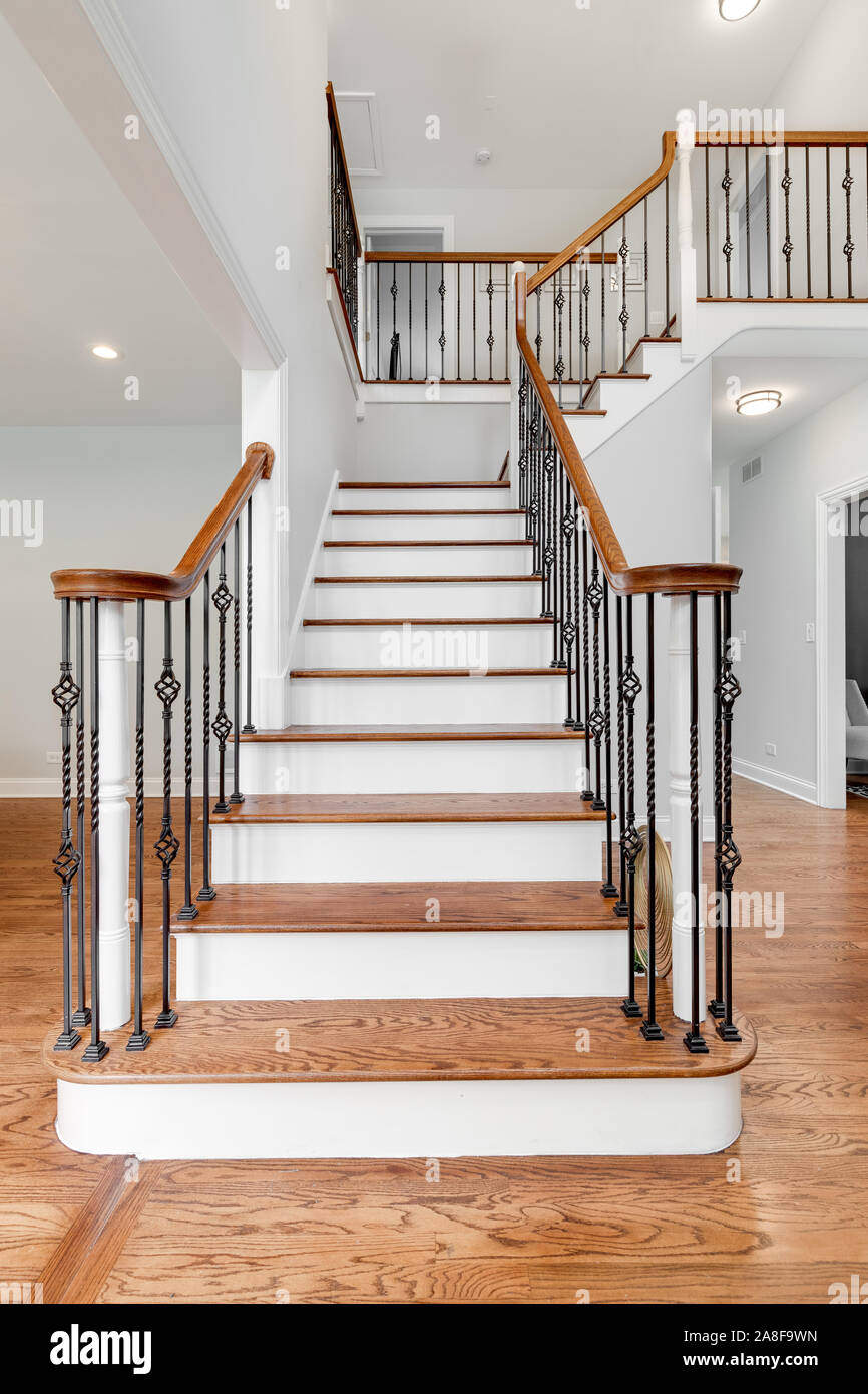 Looking up a household staircase with wrought iron railings, wood banisters, and hardwood floors throughout the house. Stock Photo