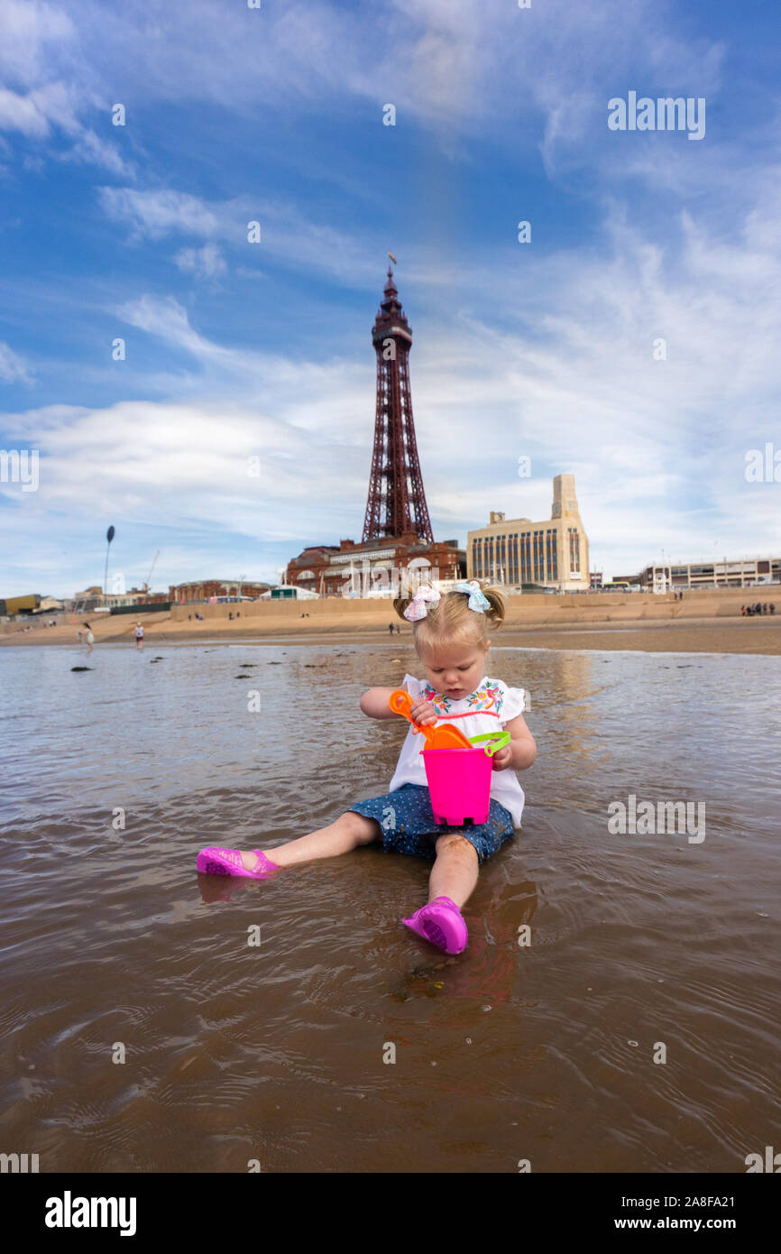 A beautiful pretty little girl sitting in the sea with her bucket and