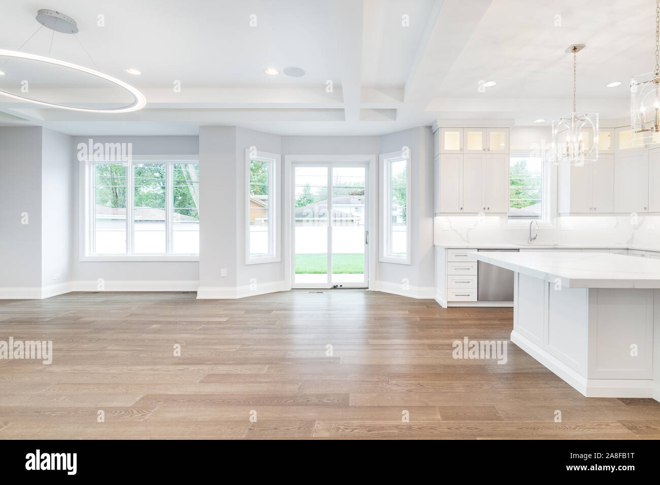 A large, empty open concept living room and kitchen with plenty of space. The luxury kitchen features white cabinets, and stainless steel appliances. Stock Photo