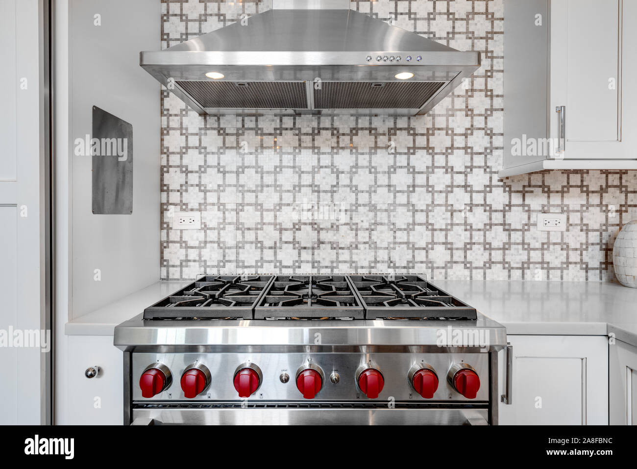 A luxury kitchen with a Wolf oven and hood with a beautiful tiled back splash surrounded by large white cabinets. Stock Photo