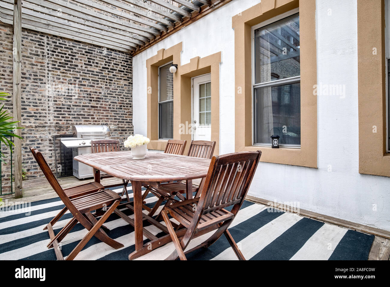 A patio in a downtown condo with a large wooden table, chairs and a stainless steel grill. Stock Photo