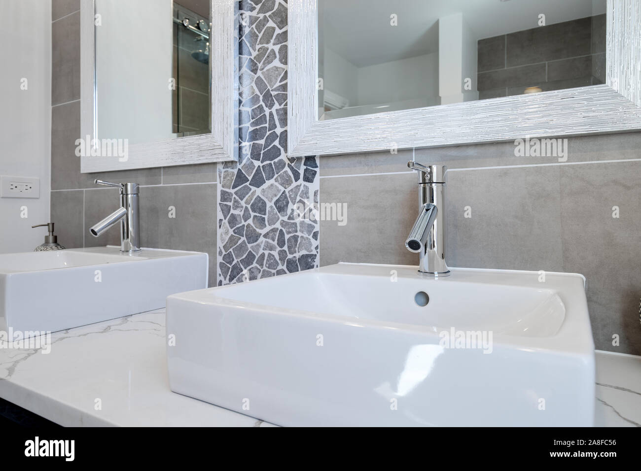 A fancy vessel sink with chrome hardware. A rock and marble back splash cover the wall with a framed mirror also hanging. Stock Photo
