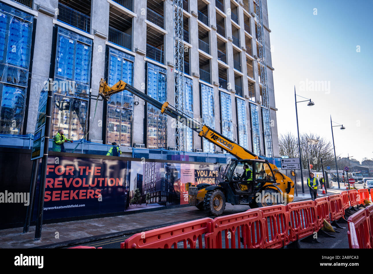 A JCB driver works on the new Hilton Hotel building, structure in Stoke on Trent, Hanley, loading and unloading materials for his work colleagues Stock Photo