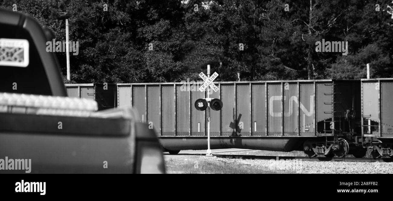 A stopped pickup truck with Confederate flag sticker waits at railroad crossing with freight train whizzing by in rural Southern Mississippi, USA, bla Stock Photo