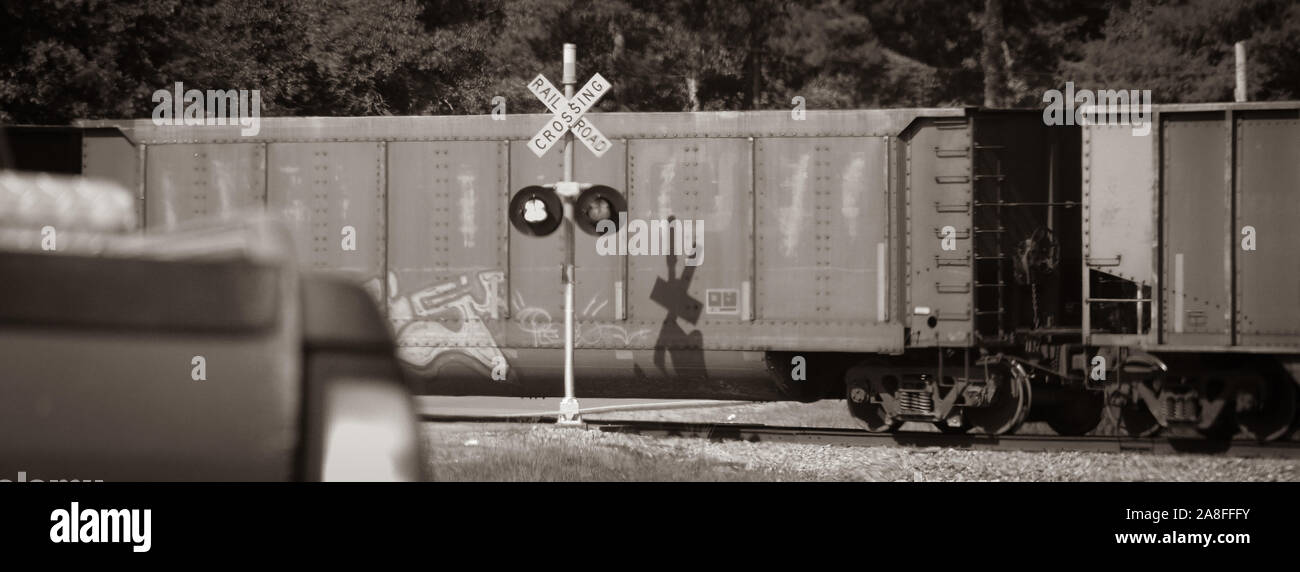 A stopped pickup truck waits at railroad crossing with blinking lights with freight train whizzing by in rural Southern Mississippi, USA, sepia toned Stock Photo