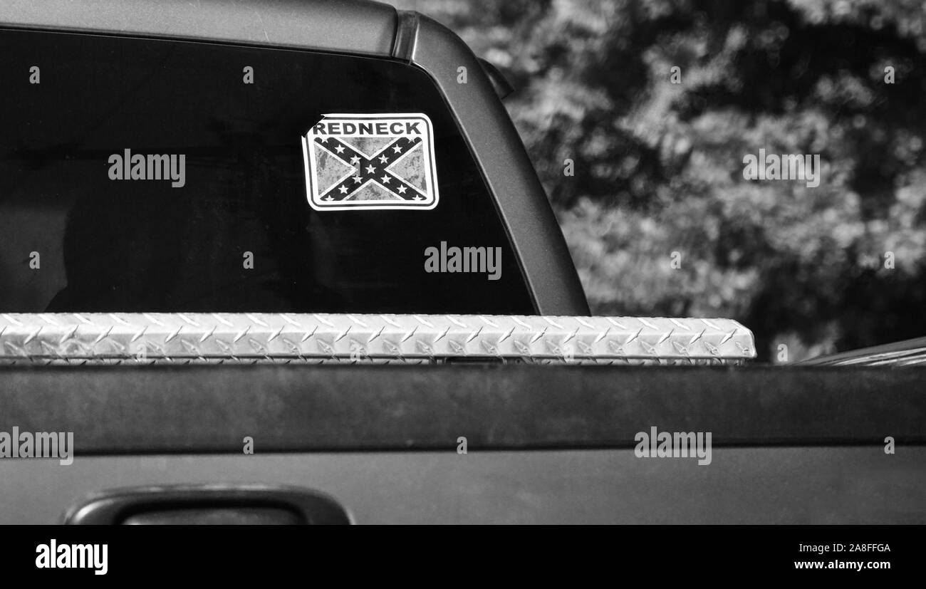 Close up of a pick up trucks rear cab window with decal sticker of the Confederate battle flag with REDNECK emblazoned with bokay  background in rural Stock Photo