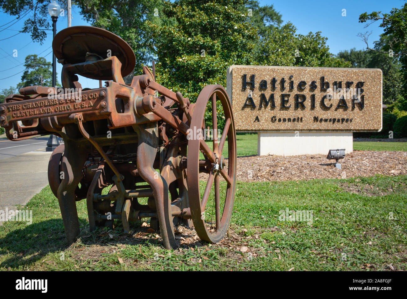 A sign for the Hattiesburg American, a Gannett Newspaper, along with a  rusty, antique printing machine are displayed in Hattiesburg, MS, USA Stock Photo