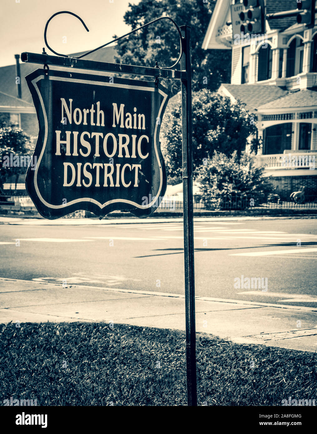 An antique style metal sign reads,  North Main Historic district, placed on the corner near Victorian Houses in Hattiesburg, MS, USA, black and white Stock Photo