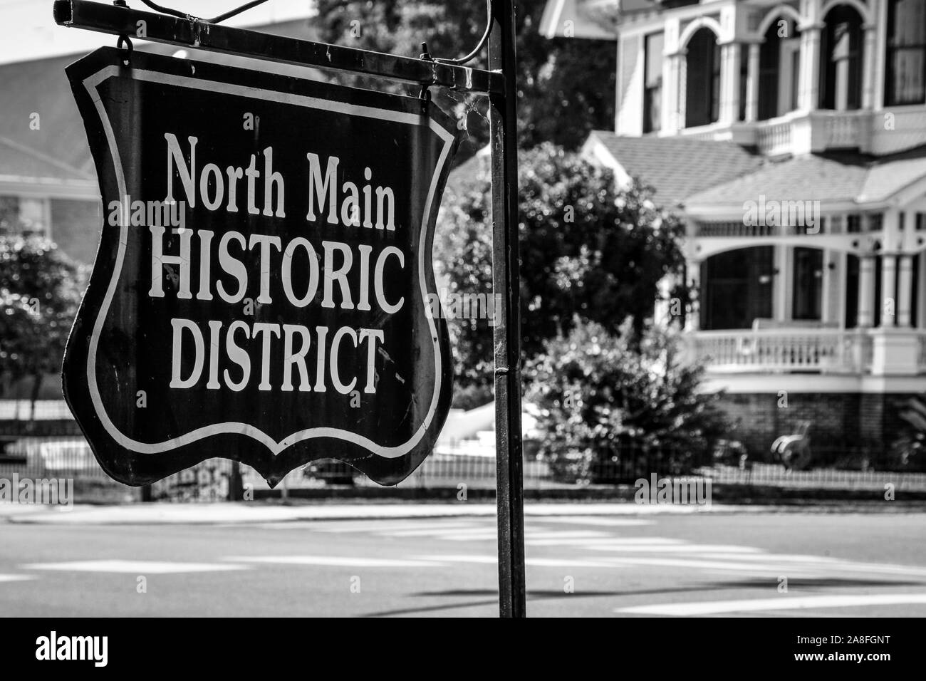 An antique style metal sign reads,  North Main Historic district, placed on the corner near Victorian Houses in Hattiesburg, MS, USA, black and white Stock Photo