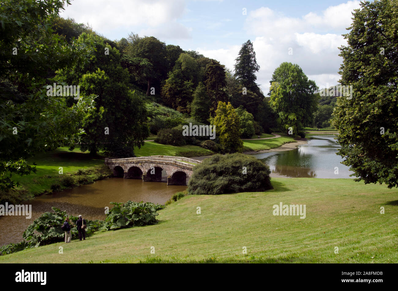 Ancient stone bridge curves over a lake in Stourhead gardens in Wiltshire UK Stock Photo