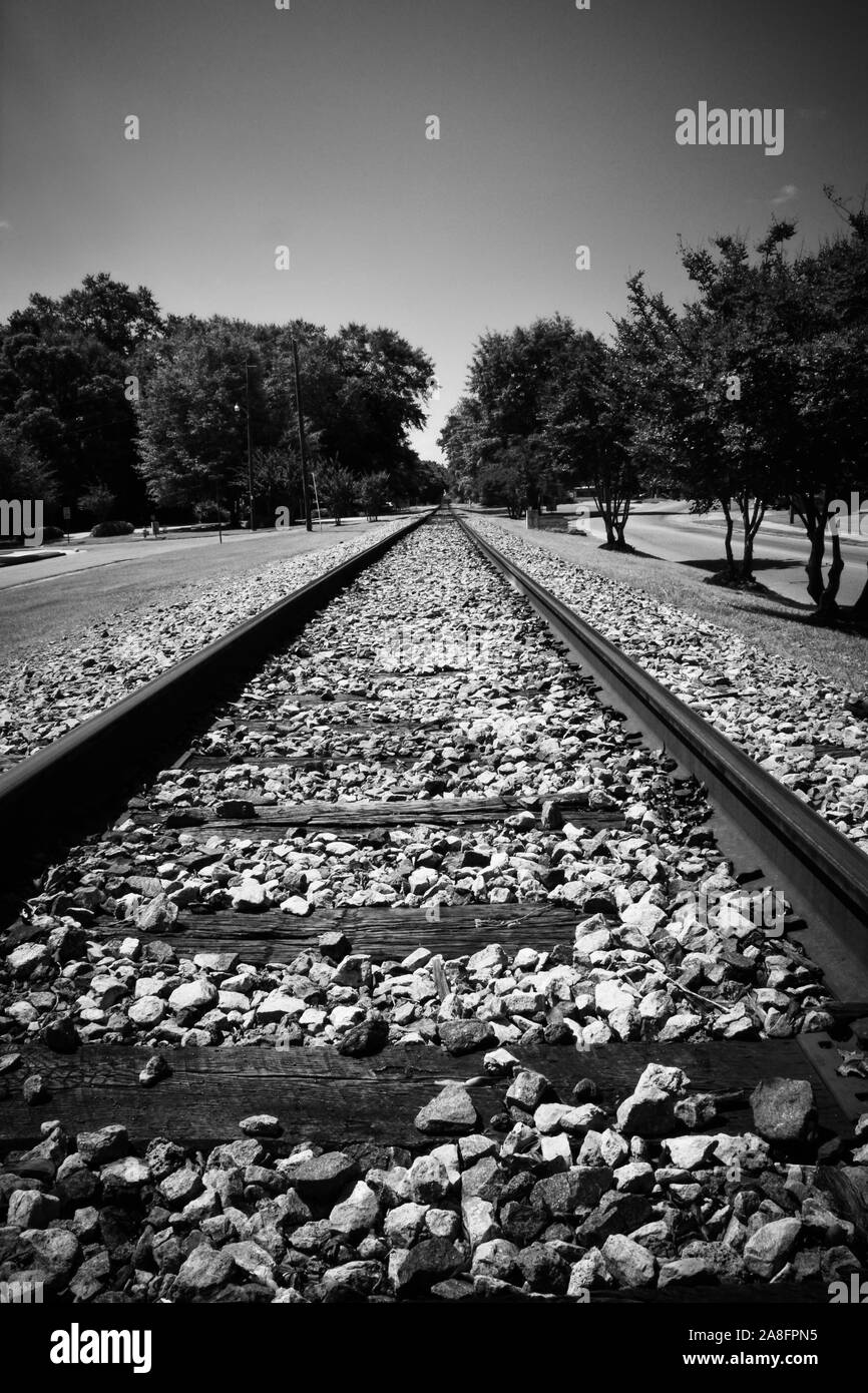 A diminishing perspective view down a straight railroad track into a wooded area in in small town America in Southern Mississippi, USA, in B & W Stock Photo