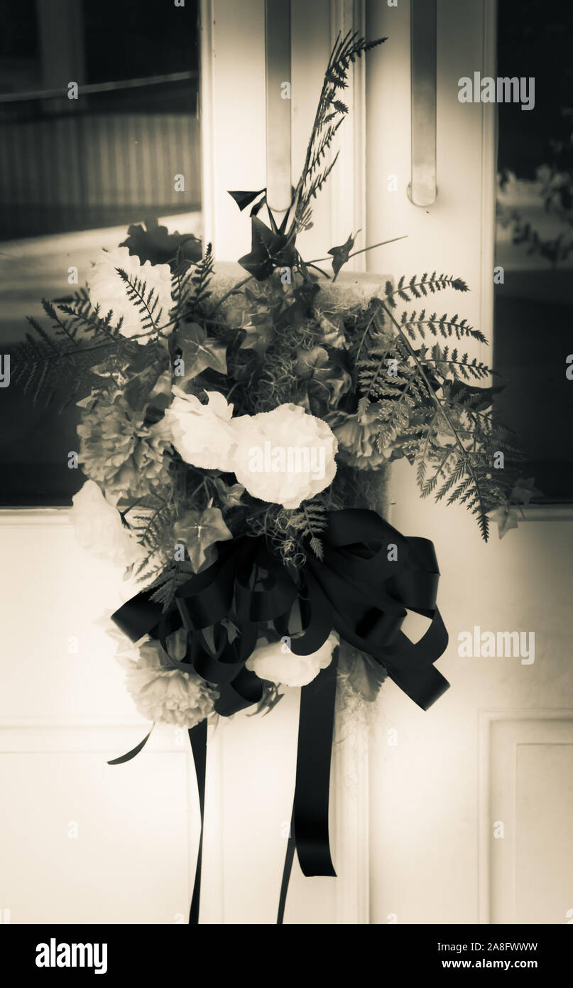 A mourning bouquet of carnations on a front door symbolizes  sympathy for the deceased family members in small town America, USA, in black and white Stock Photo