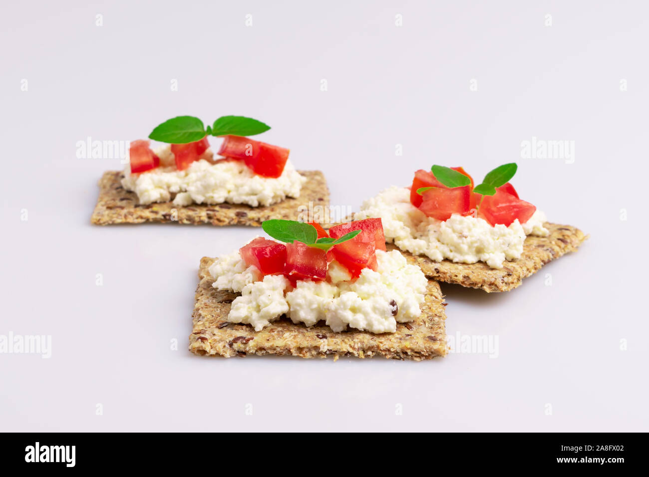 Diet flax seed whole grain crackers with ricotta cheese, tomato and herbs isolated on white background, soft light Stock Photo