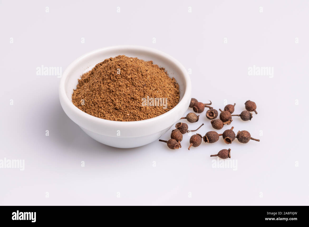 Ground allspice in white ceramic bowl isolated on white background, soft light, studio shot, copy space.  Also called Jamaica pimenta, or myrtle peppe Stock Photo