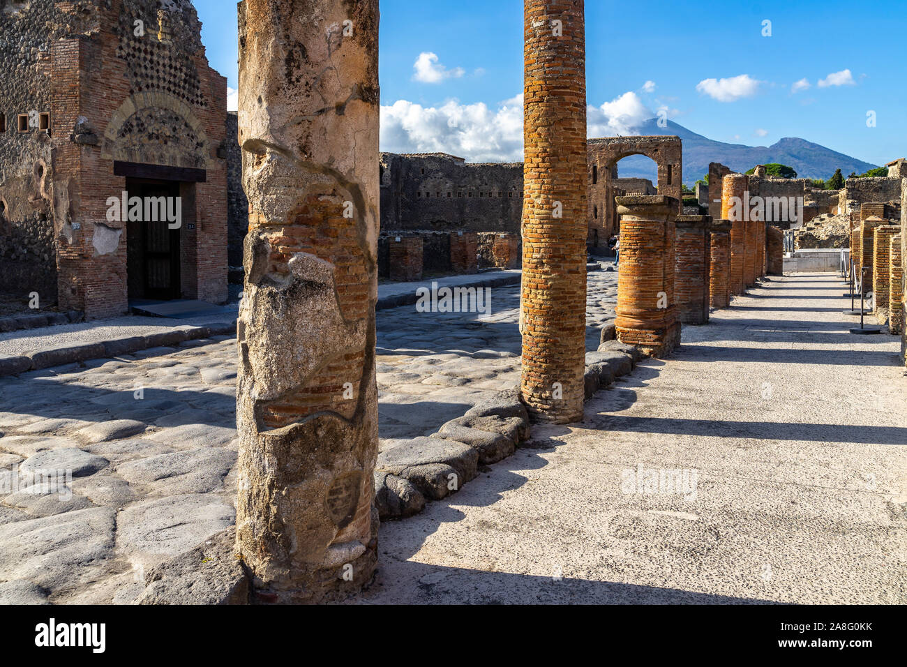 Ruins of Roman columns in Pompeii along Via del Foro with Arch of Caligula and Mount Vesuvius in the background, Italy Stock Photo