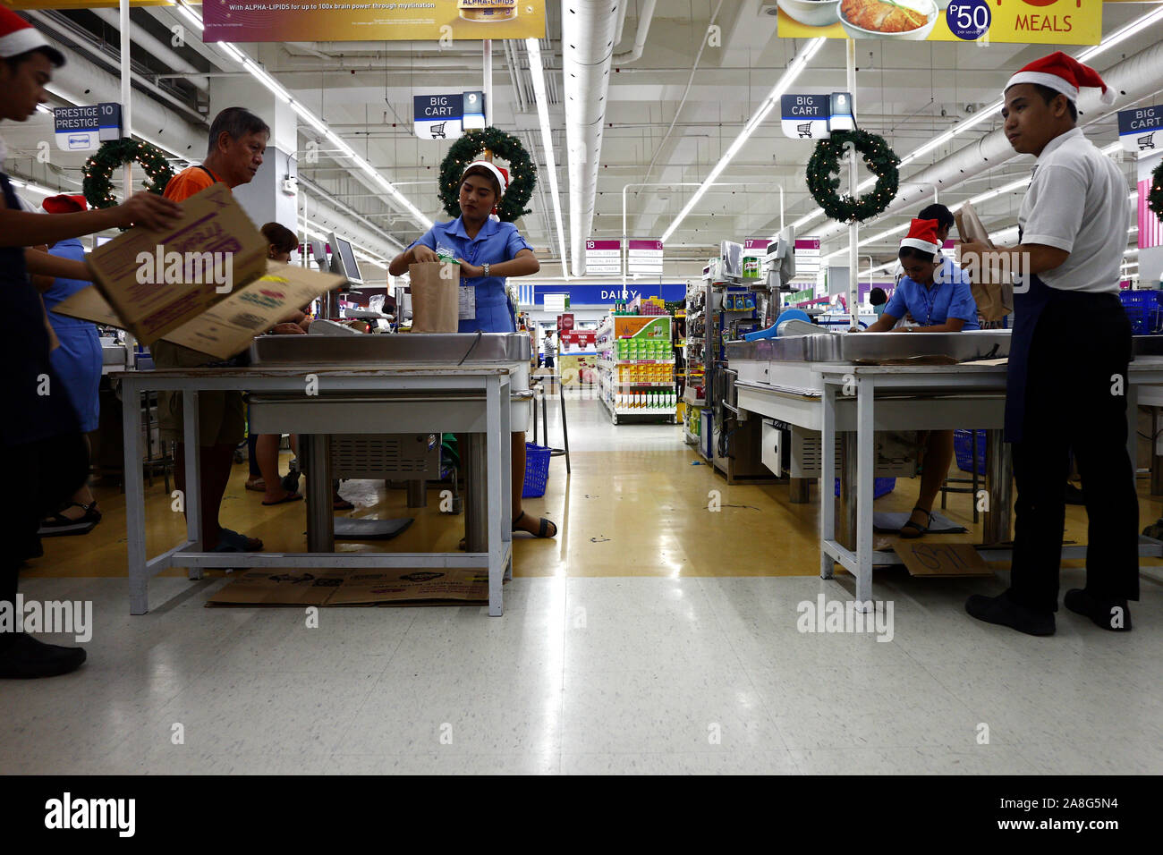 PASIG CITY, PHILIPPINES – NOVEMBER 3, 2019: Employees of a grocery store serve customers at the cashier or check out counter. Stock Photo