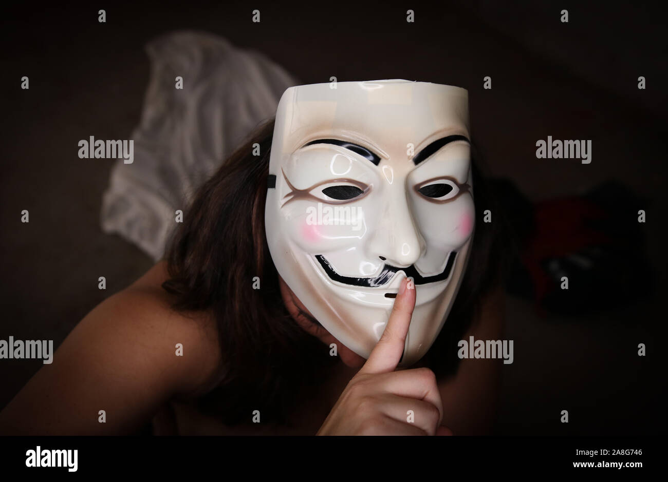 Revolution and Reform. Anti-establishment and rebellion. A girl wears a Guy Fawkes mask and holds a finger up that silence the viewer. Stock Photo