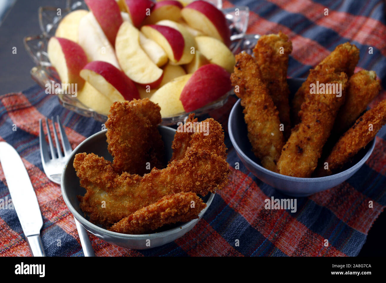 Photo of freshly cooked crispy chicken and fish strips and bowl of sliced apple and pear Stock Photo