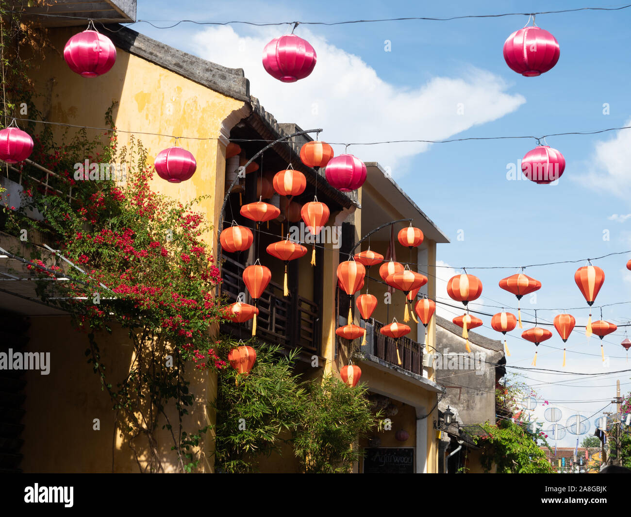 Fabric lanterns in orange and fuchsia strung between gold stucco buildings in the old city of Hoi An, Vietnam. Stock Photo