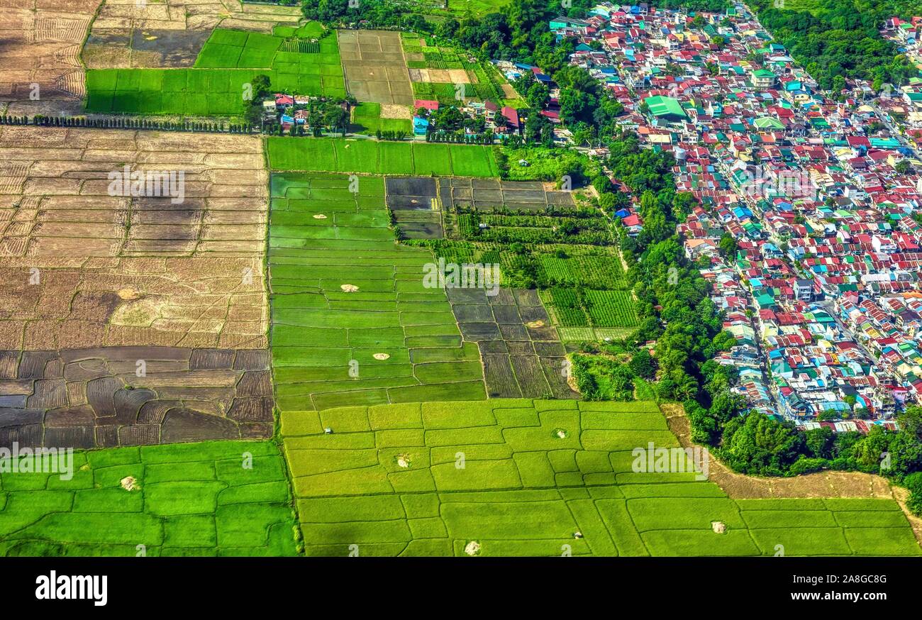 Aerial view showing expansion of urbanization and mass housing into agricultural land and rice fields in southeast Asia. Luzon island, Philippines. Stock Photo