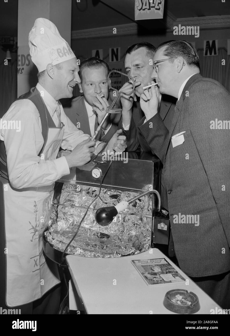 Three men have their cigarettes lit by the barbeque chef at a sporting goods convention in Southern California, ca. 1955. Stock Photo
