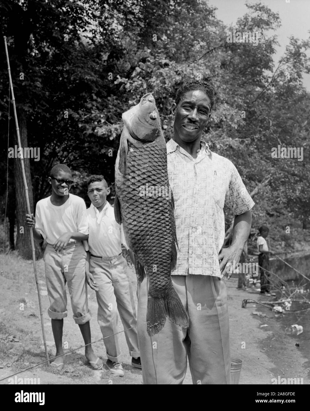 A man holds up an 18 lb carp he caught in Douglas Park Lagoon in Chicago, Illinois ca. 1966 Stock Photo